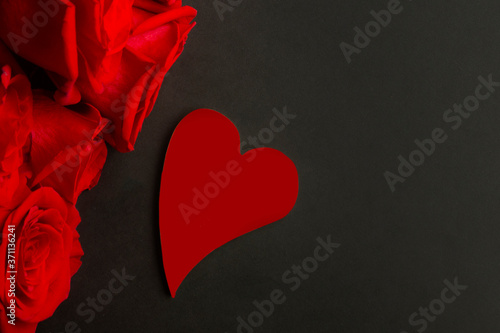 Heap of fresh red roses in full bloom and Red heart on black background, close up. Bunch of flowers. Copy space. flat lay. Valentine's day or Mother's day, love concept.