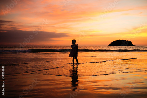 Happy child girl black silhouette on sun background. Kid having fun by water pool along sea on beach. Travel lifestyle, summer vacation.