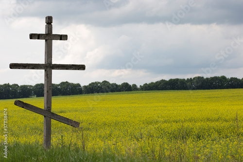 Old wooden Orthodox cross on a rapeseed field in Ukraine. Symbol of the Christian religion. Rural landscape. Summer. July.
