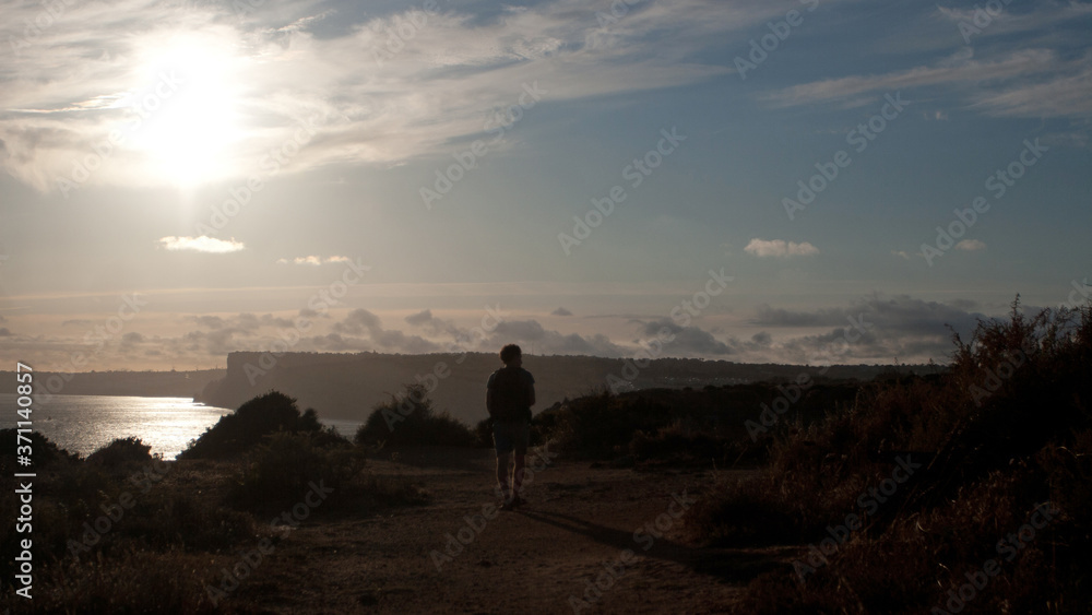 Male silhouette in the sunset walking down to the sea
