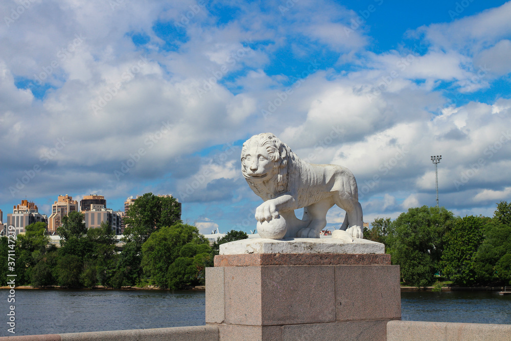 Obraz premium History and modernity - a white lion statue and a modern residential complex against the backdrop of a blue sky with clouds. St. Petersburg.