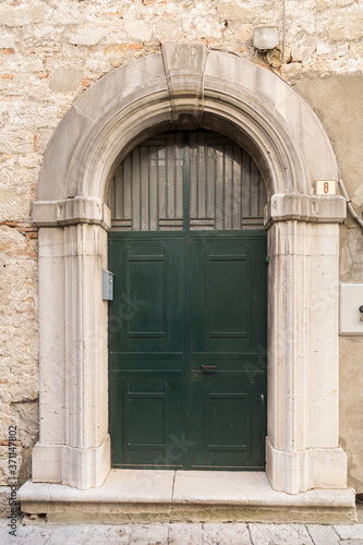 External daytime photo of a recent iron door carved out of a medieval carved stone decorated door in Venosa in the Basilicata region of southern Italy