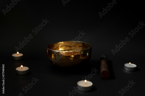A Tibetan singing bowl on a black background surrounded by candles. Minimal design.