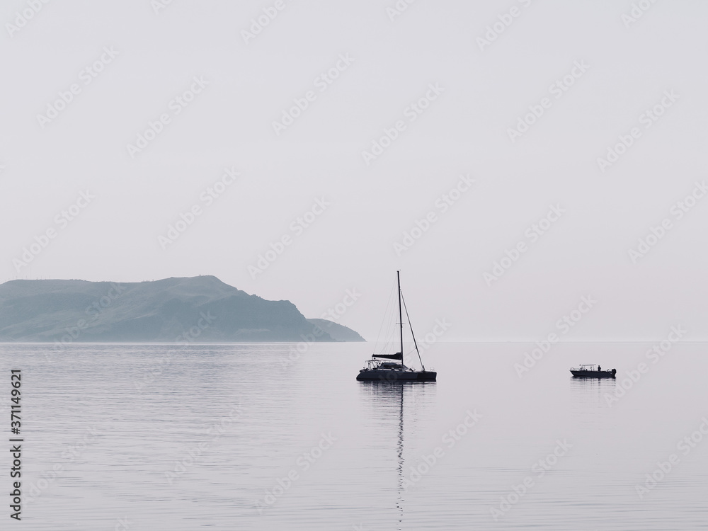 Minimal view of the sea, Crimea. Morning seascape with a lonely boat floating in the middle of the sea and overlooking the mountains in the haze. Minimalism. Minimal view of the sea, Crimea. Morning seascape with a lonely boat floating in the middle of the sea and overlooking the mountains in the haze. Minimalism.