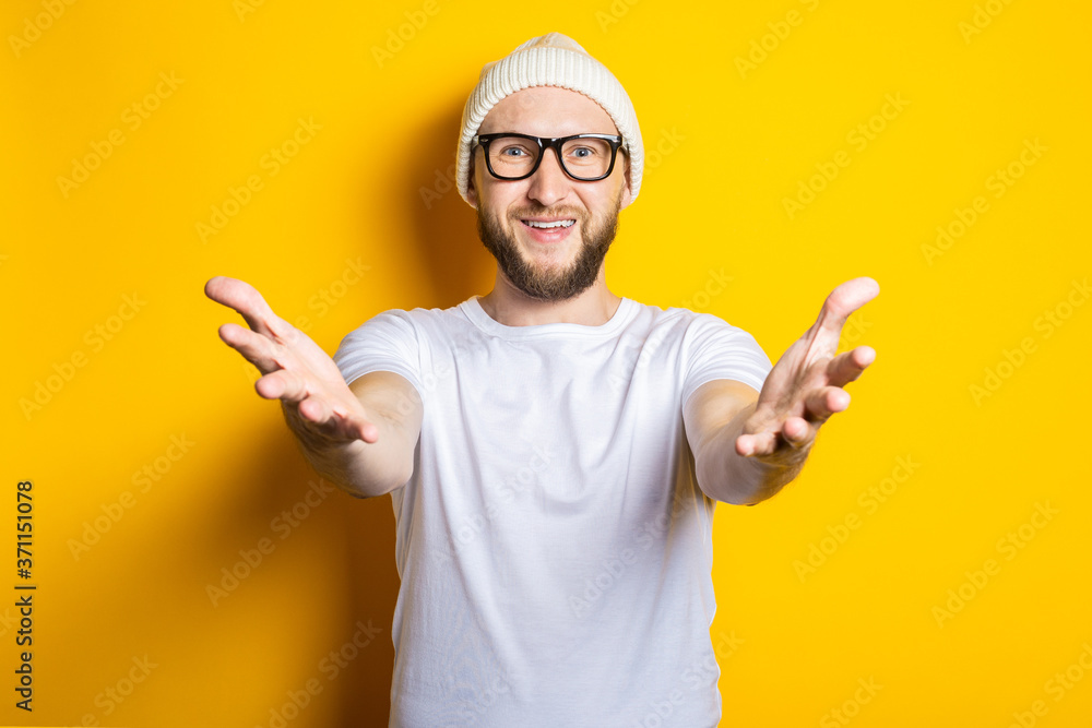 Smiling bearded young man happily pulls his hands to the camera, going to hug on a yellow background. Smiling bearded young man happily pulls his hands to the camera, going to hug on a yellow background.