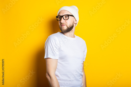 Handsome young man with beard in hat and glasses on yellow background.