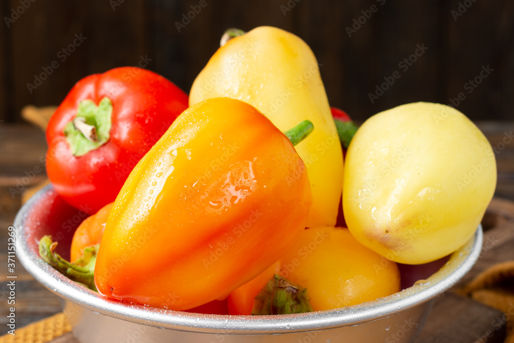 Sweet pepper. Red and yellow peppers in a metal bowl on a brown wooden table. Pepper close up