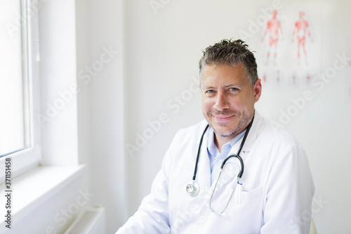 Portrait of a good looking male doctor in his office with a three-day beard and white coat