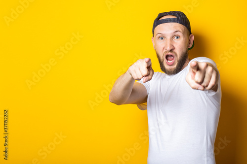 Screaming young man in white t-shirt pointing with fingers in front of him on yellow background.