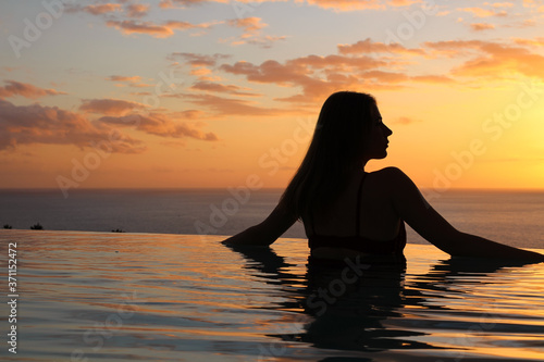 Silhouette of a girl with long loose hair,who stands at the edge of the pool and looks at the sunset and the ocean. hotel Las Terrazas de Abama © Elena