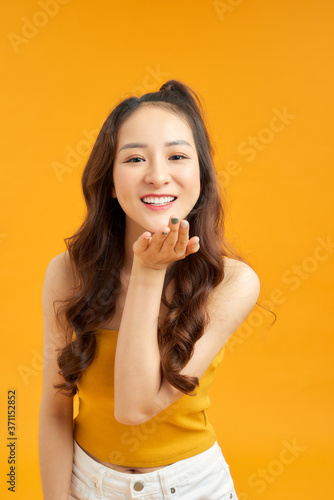 Pretty friendly girl blowing air kiss at camera isolated on yellow background