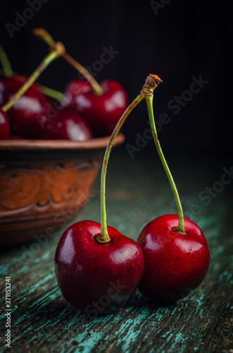 Clay plate with ripe red cherries on a wooden old table.