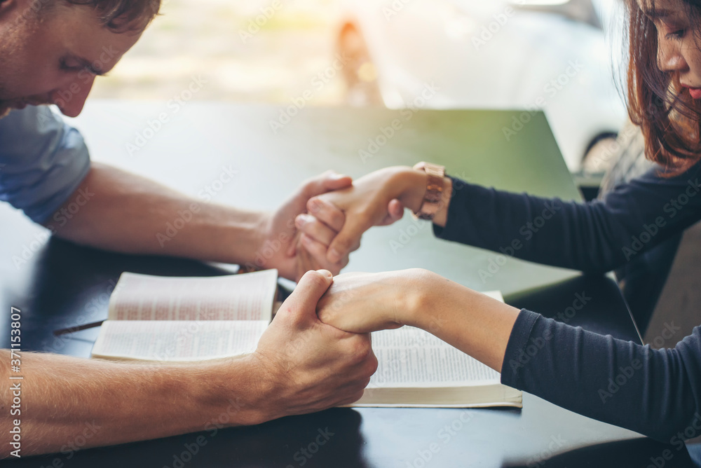 Obraz premium Pray and bible concept.Asian female praying,hope for peace and free from disease,Hand in hand together by woman and Caucasian men,believes and faith in christian religion at church.