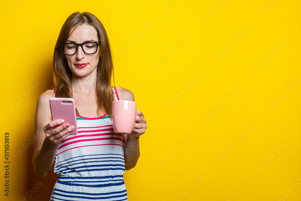 Young woman in focus looking phone, holding a cup with coffee on a yellow background. Young woman in focus looking phone, holding a cup with coffee on a yellow background.