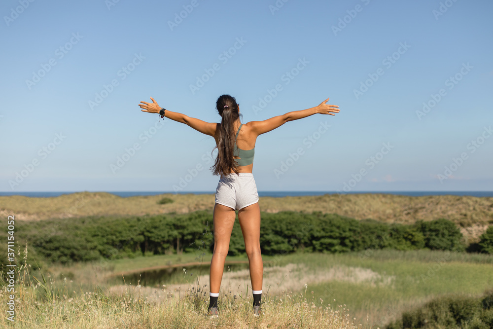 Healthy fitness lifestyle success. Back view of sporty blissful fit young woman raising arms to the sky.sporty young woman raising arms Healthy fitness lifestyle success. Back view of sporty blissful fit young woman raising arms to the sky.sporty young woman raising arms