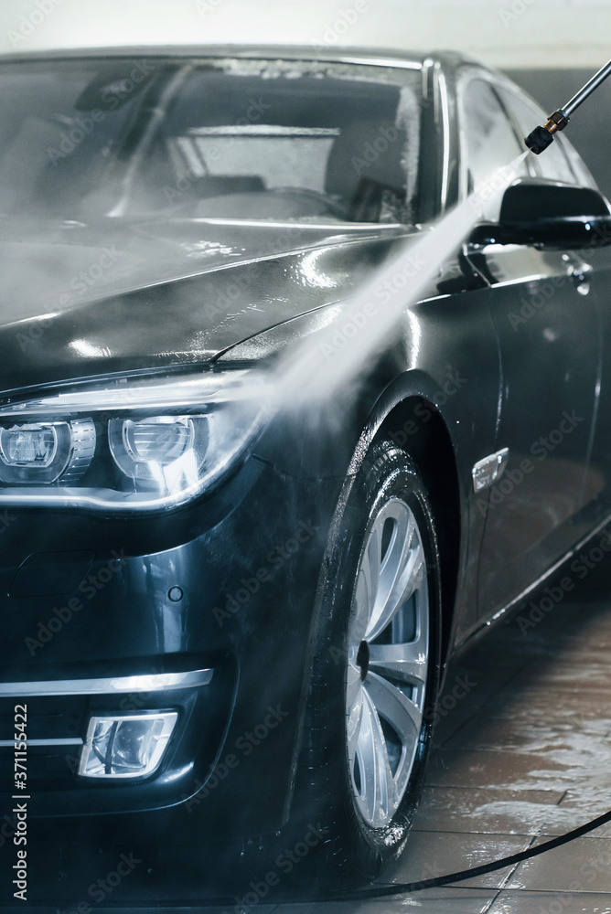 High pressured water. Modern black automobile get cleaned inside of car wash station