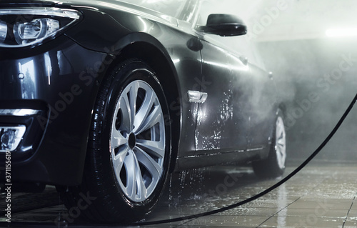 High pressured water. Modern black automobile get cleaned inside of car wash station © standret
