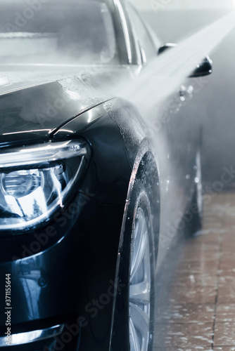 High pressured water. Modern black automobile get cleaned inside of car wash station