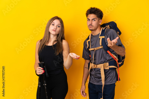 Young mountaineer couple with a big backpack isolated on yellow background unhappy and frustrated with something because not understand something