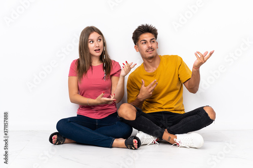 Young couple sitting on the floor isolated on white background extending hands to the side for inviting to come