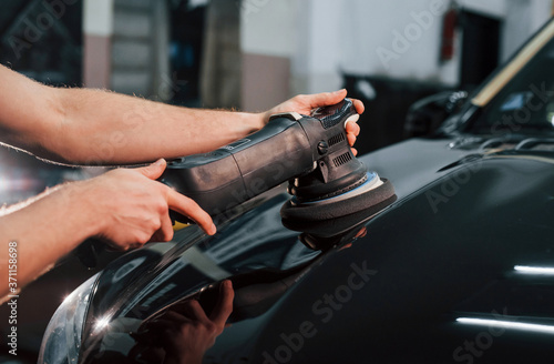 Guy polishing surface of vehicle. Modern black automobile get cleaned by man inside of car wash station