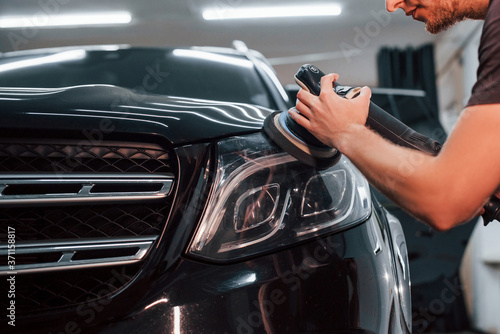 Guy polishing surface of vehicle. Modern black automobile get cleaned by man inside of car wash station © standret