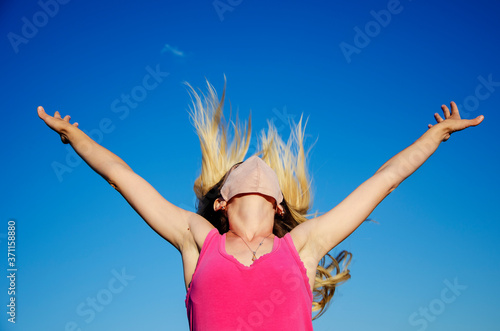 Happy girl takes off the mask against the blue sky. Freedom, happiness, joy. The girl jumped up with joy. End of quarantine and general removal of masks
