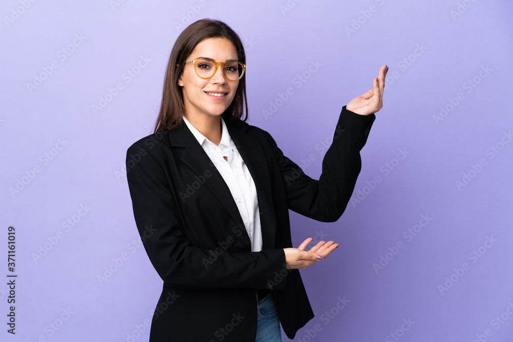 Business woman isolated on purple background extending hands to the side for inviting to come Business woman isolated on purple background extending hands to the side for inviting to come