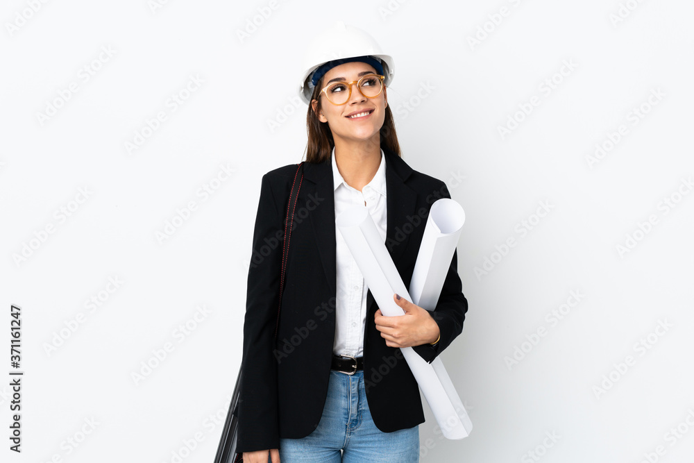 Young architect caucasian woman with helmet and holding blueprints over isolated background laughing and looking up Young architect caucasian woman with helmet and holding blueprints over isolated background laughing and looking up