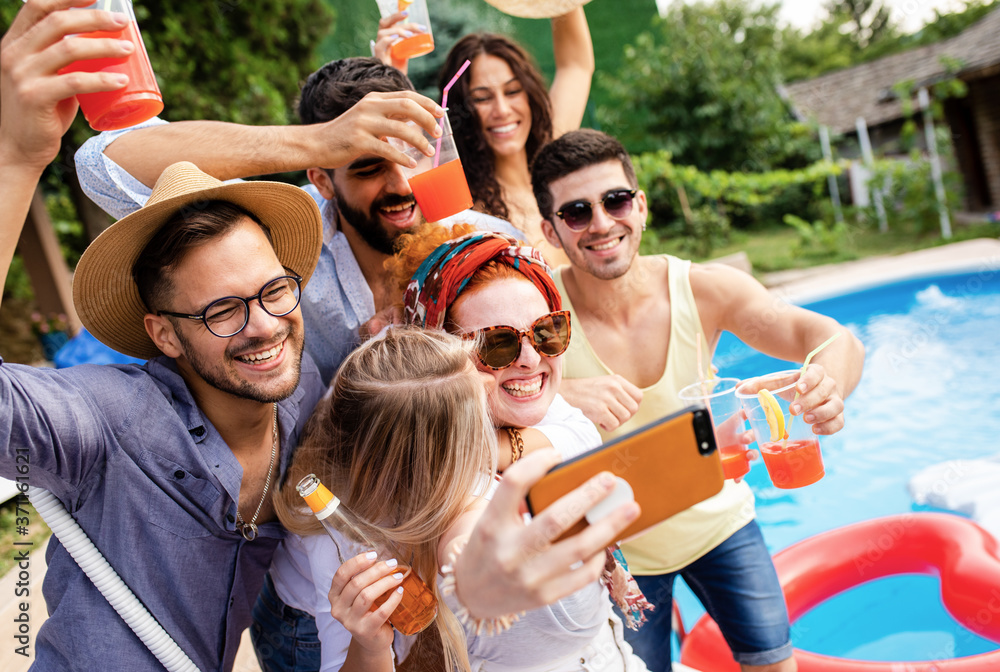 Obraz premium Group of young people having fun at summer vacation and enjoying a poolside party with drinks and making selfie.