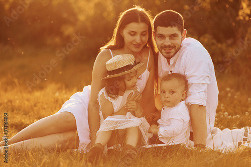Sitting on the grass. Father, mother with daughter and son spending free time outdoors at sunny day time of summer