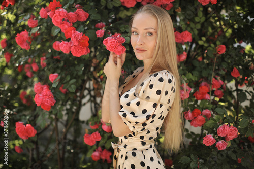 Portrait of a young beautiful woman in dress in roses flowers outdoor