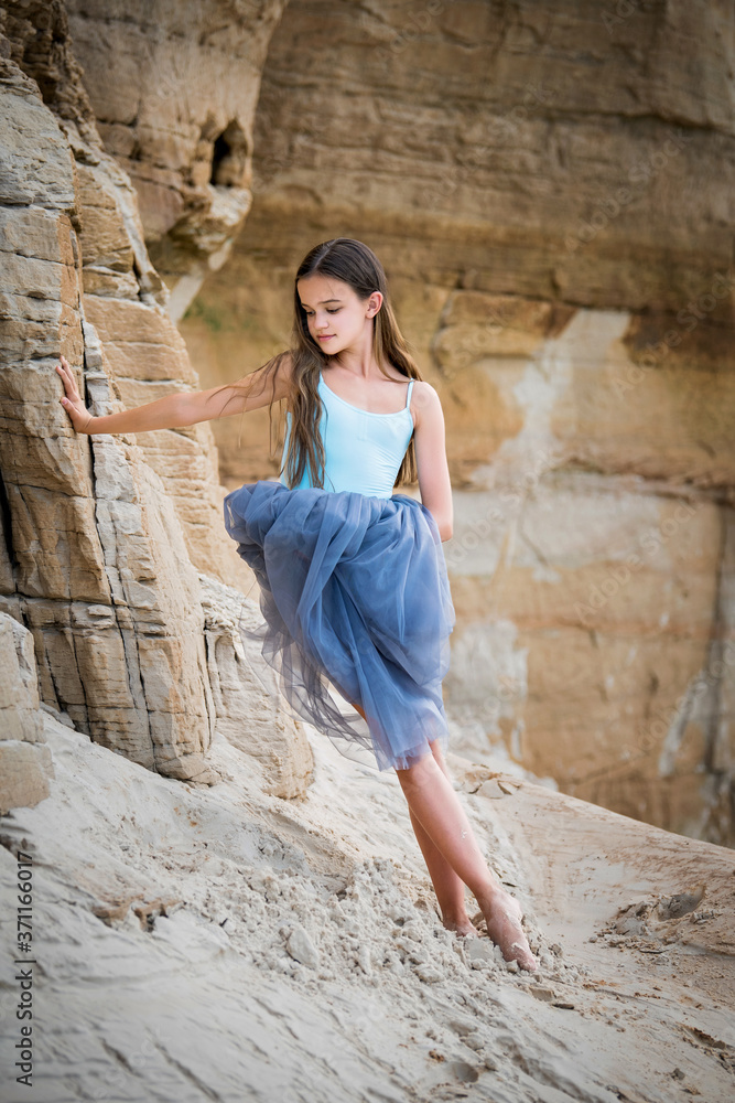 young ballerina stands in a graceful pose on the edge of a sandy cliff against the background of the lake