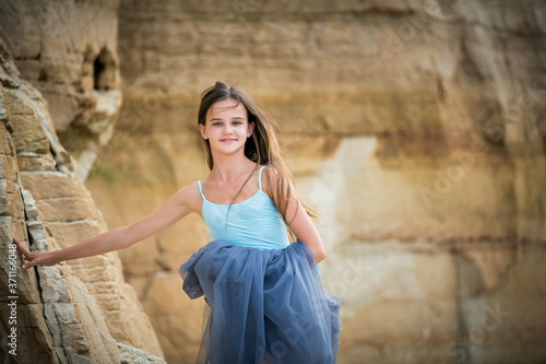 portrait of a ballerina in a light blue dress stands against the background of high sandy cliffs © Maria Moroz
