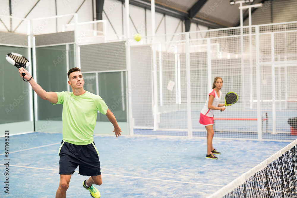 Couple playing paddle tennis in blue cour