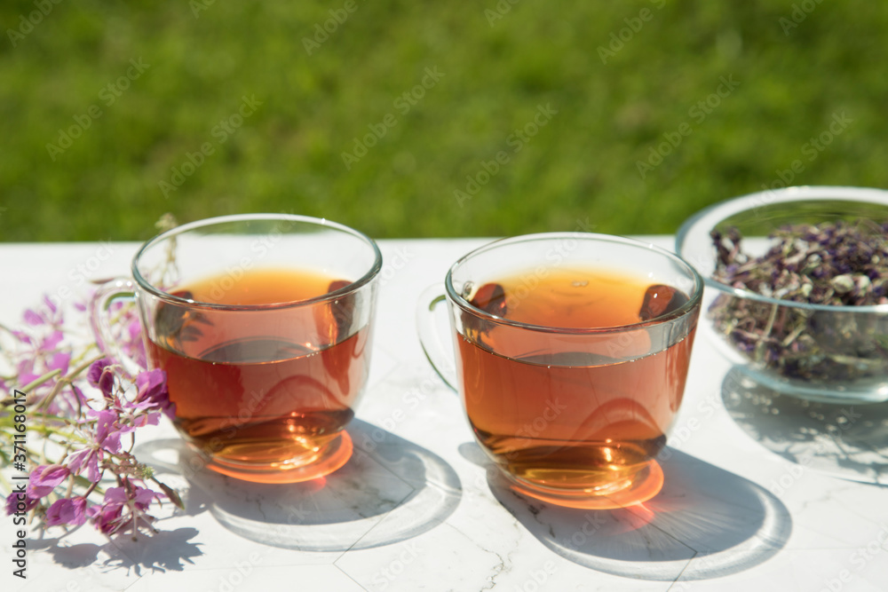 Chamaenerion angustifolium tea (Cypress, pink willow, Ivan-tea) with dry and fresh flowers for decoration in two glass cups on a light background . Concept of herbal medicine. Chamaenerion angustifolium tea (Cypress, pink willow, Ivan-tea) with dry and fresh flowers for decoration in two glass cups on a light background . Concept of herbal medicine.