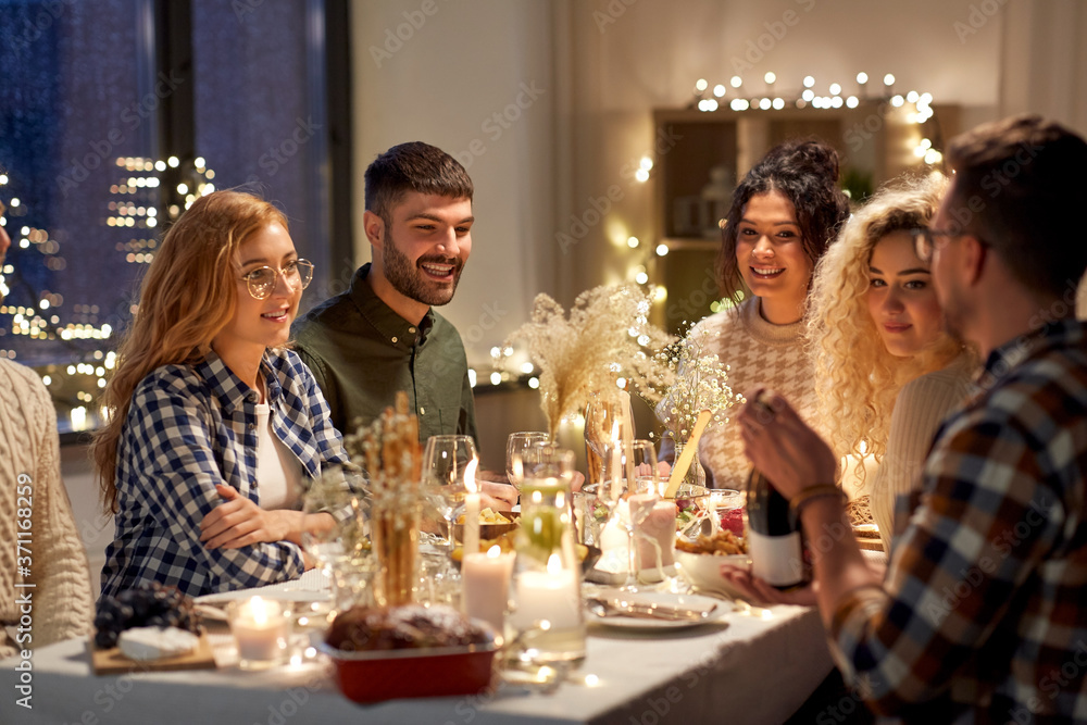 holidays and celebration concept - happy friends having christmas dinner at home with bottle of non-alcoholic red wine holidays and celebration concept - happy friends having christmas dinner at home with bottle of non-alcoholic red wine