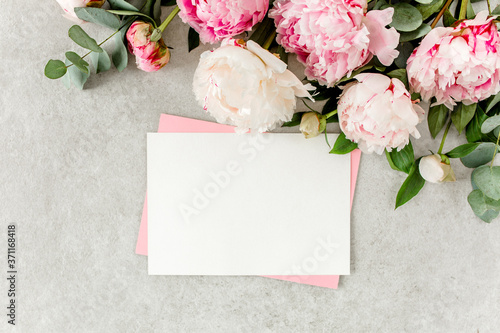 Mockup invitation  blank paper greeting card  pink envelope and peonies on gray stone table. Flower background. Flat lay  top view.