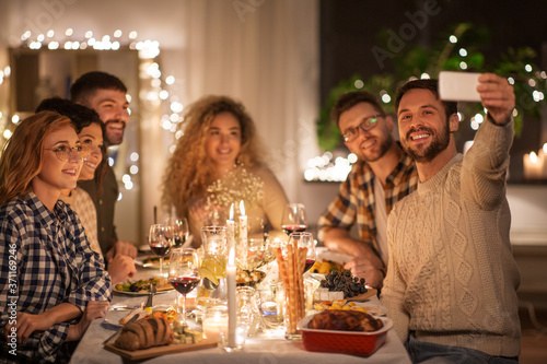holidays, celebration and people concept - happy friends taking selfie by smartphone at home christmas dinner party
