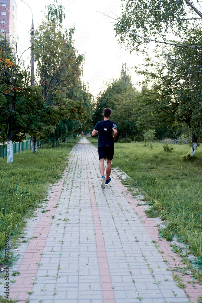 Man is running on empty street in the park on early morning back view