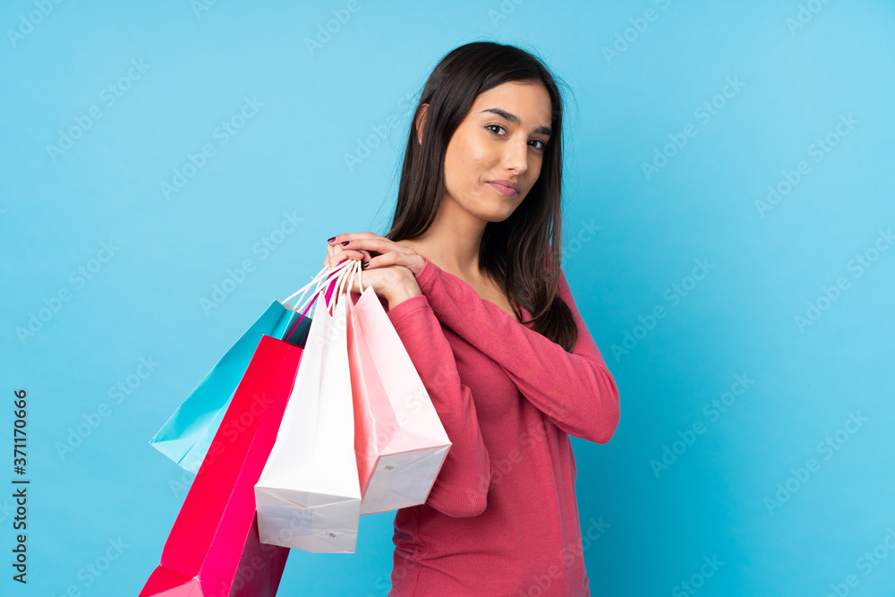 Young brunette woman over isolated blue background holding shopping bags Young brunette woman over isolated blue background holding shopping bags