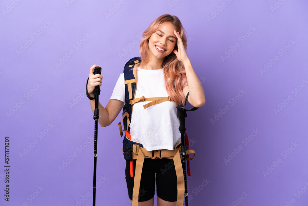 Teenager girl with backpack and trekking poles over isolated purple background smiling a lot