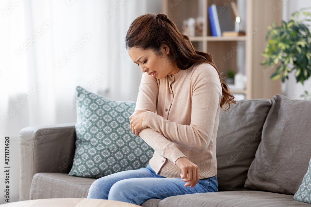 people and health problem concept - unhappy asian woman suffering from pain in hand at home people and health problem concept - unhappy asian woman suffering from pain in hand at home