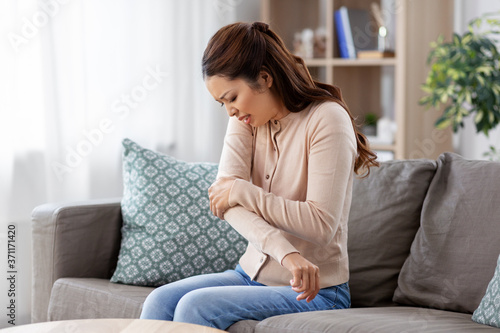 people and health problem concept - unhappy asian woman suffering from pain in hand at home