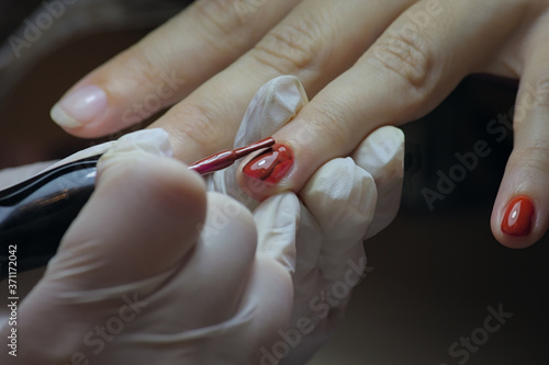 Manicure process. The master applies red gel polish to women s nails. Local lighting. Selective focus