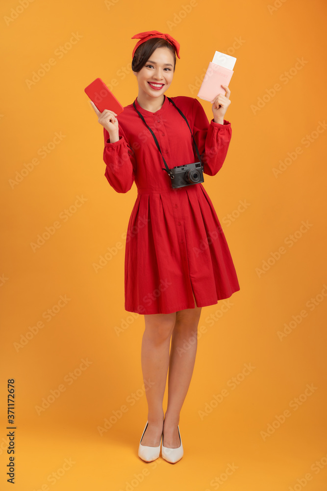 Happy tourist woman in summer red dress holding passport isolated on orange background. Happy tourist woman in summer red dress holding passport isolated on orange background.