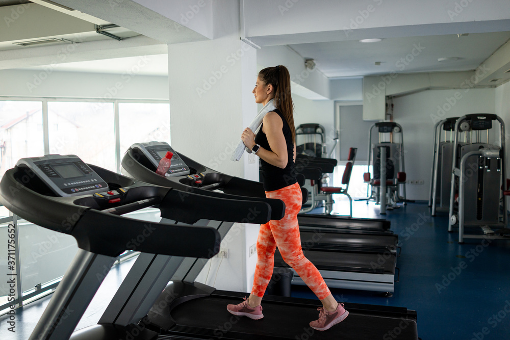Pretty fit woman running on treadmill in gym