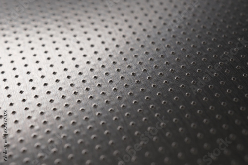 Dark industrial metallic background or wallpaper. Perforated aluminum surface with many holes. Perforation rows go into the distance and form a perspective. Macro