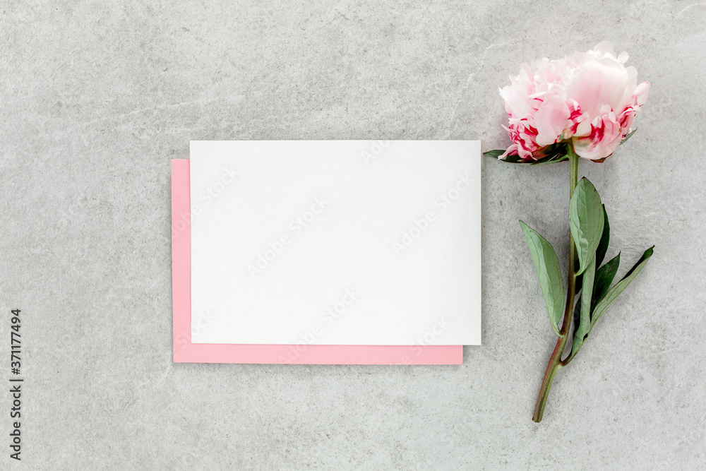 Mockup invitation, blank paper greeting card, pink envelope and peonies on gray stone table. Flower background. Flat lay, top view. Mockup invitation, blank paper greeting card, pink envelope and peonies on gray stone table. Flower background. Flat lay, top view.