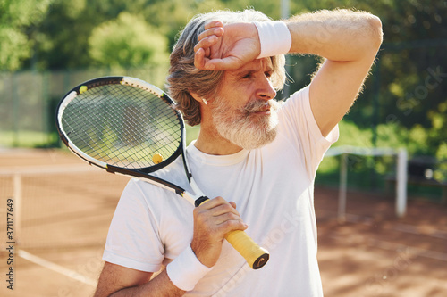 Senior modern stylish man outdoors on the tennis coart at daytime and holding racket © standret